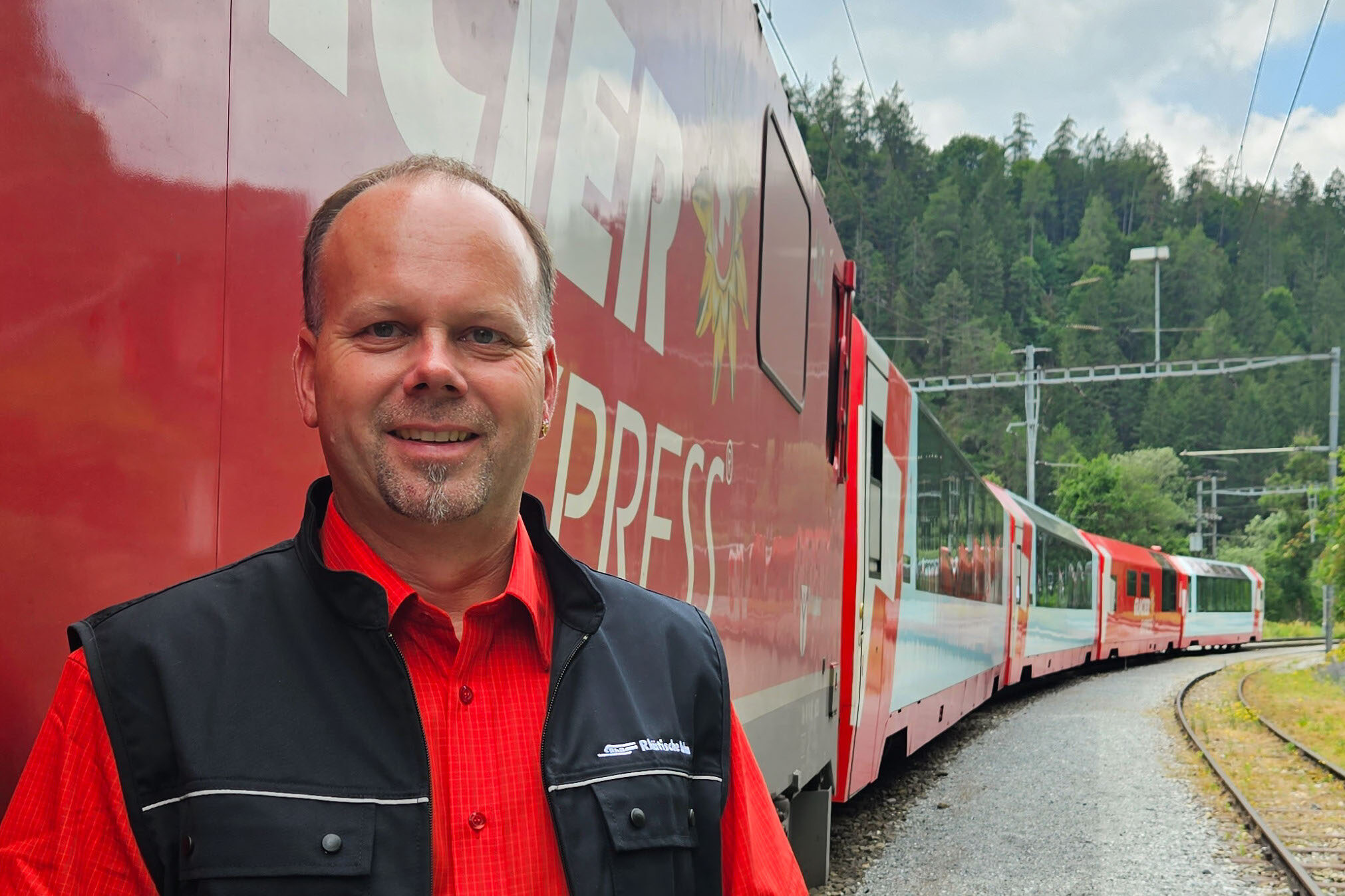 Der Lokführer Martin Koch steht vor einem Zug der Rhätischen Bahn und lacht in die Kamera.